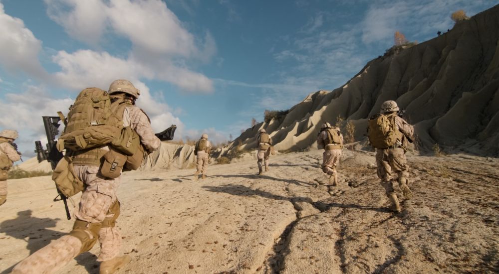 Soldiers in Iraq War advancing uphill under clear skies, showcasing military readiness and teamwork.