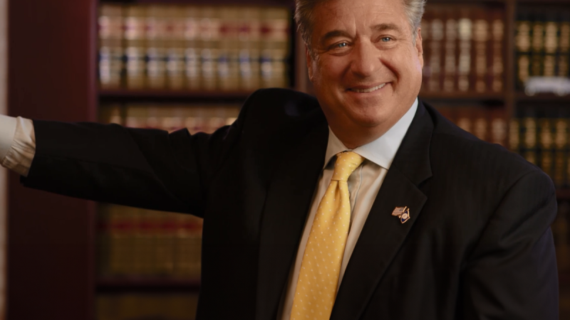Smiling businessman in a suit and yellow tie in a library office setting.