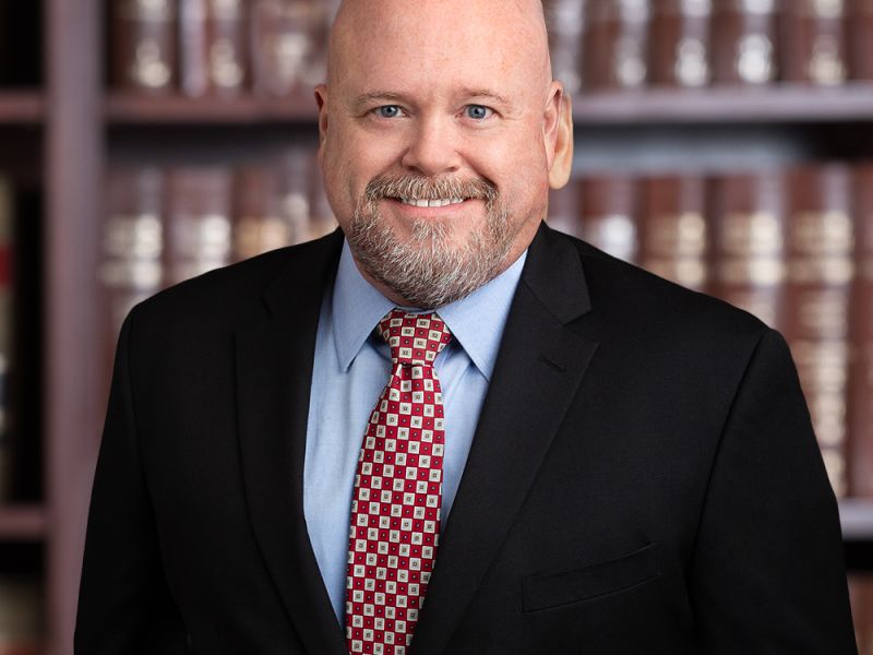 Business professional in suit smiling in front of bookshelves. Ideal for corporate or legal website.