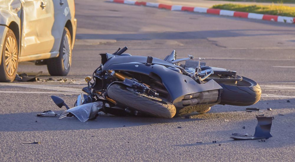 Motorcycle and car collision on road with damaged vehicles and debris scattered around, highlighting traffic accident scene.