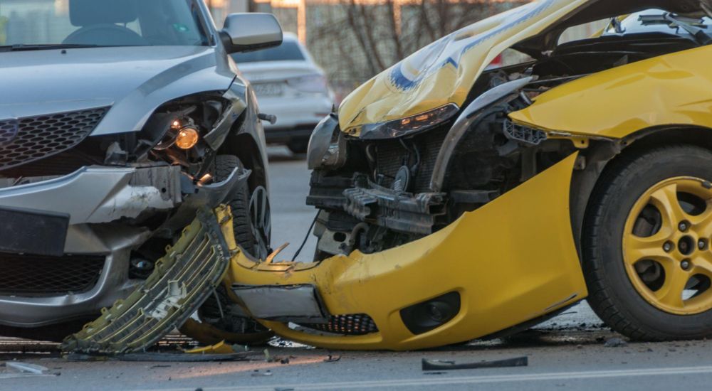 Two cars in a front-end collision on a city street, showing significant damage to both vehicles.