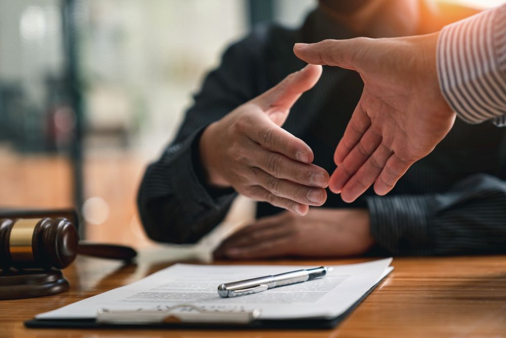 Handshake sealing a legal agreement, with contract and gavel on table, signifying a successful business deal.