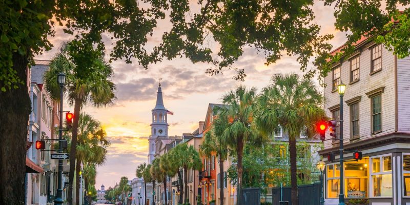 Historic street in Charleston with church, palm trees, and sunset sky.