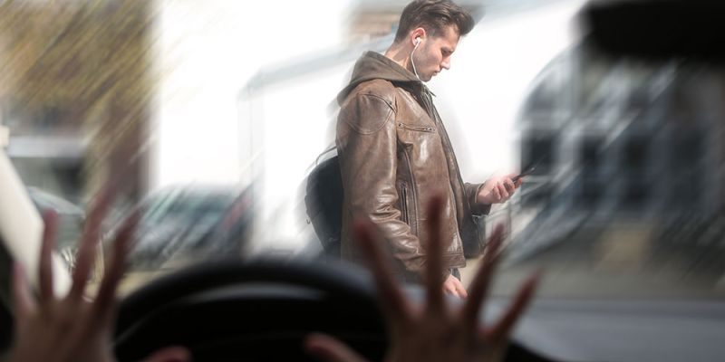 Pedestrian using phone while crossing street, viewed from car driver's perspective, highlighting road safety issues.