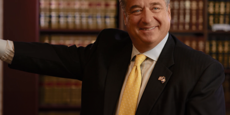 Smiling businessman in a suit and yellow tie in a library office setting.