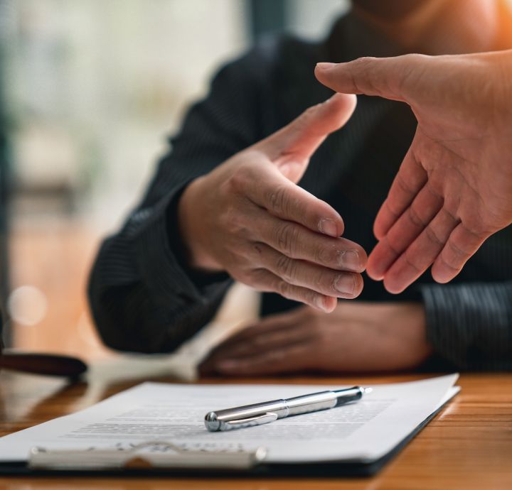 Handshake sealing a legal agreement, with contract and gavel on table, signifying a successful business deal.