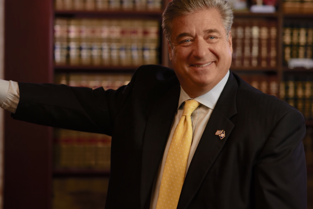 Smiling businessman in a suit and yellow tie in a library office setting.