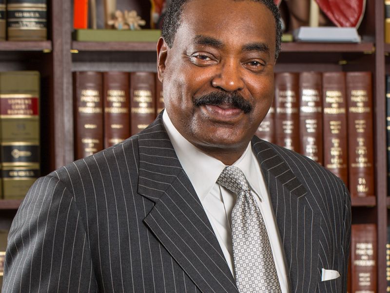 Professional man in a suit smiling in front of bookshelves with anatomical models, conveying expertise and knowledge.