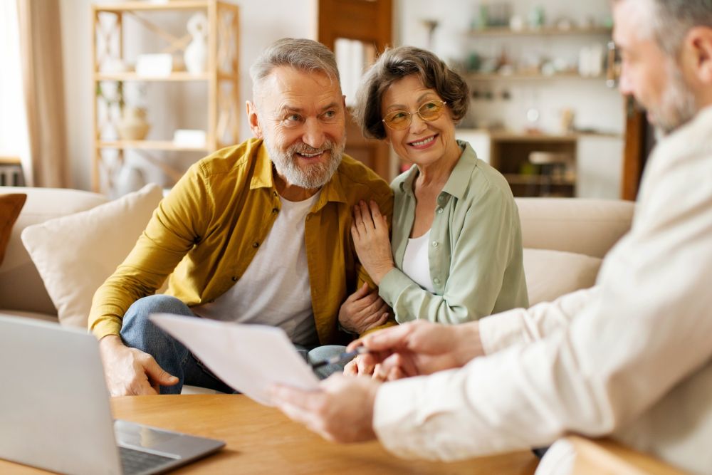 Senior couple consulting with advisor at home, smiling and reviewing documents.