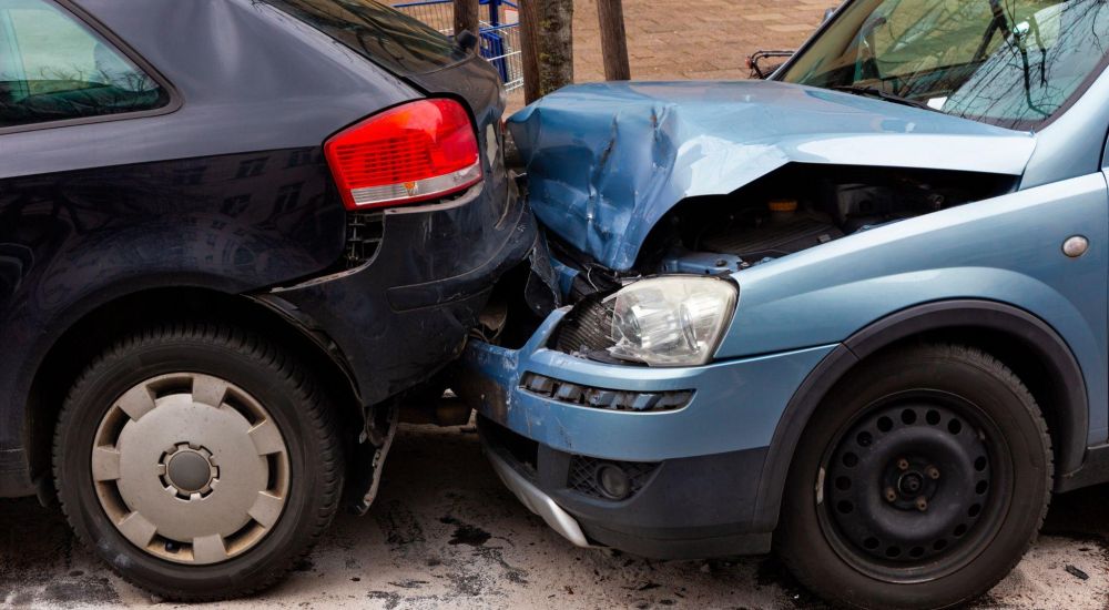 Two cars in a rear-end collision on a street, showcasing crash damage and road safety concerns.