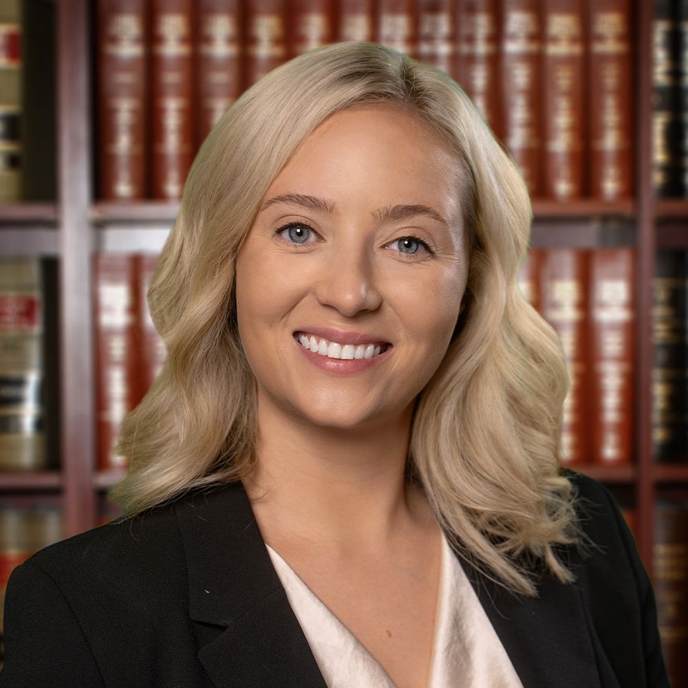 Smiling professional woman in suit with bookshelves in the background, conveying confidence and expertise.