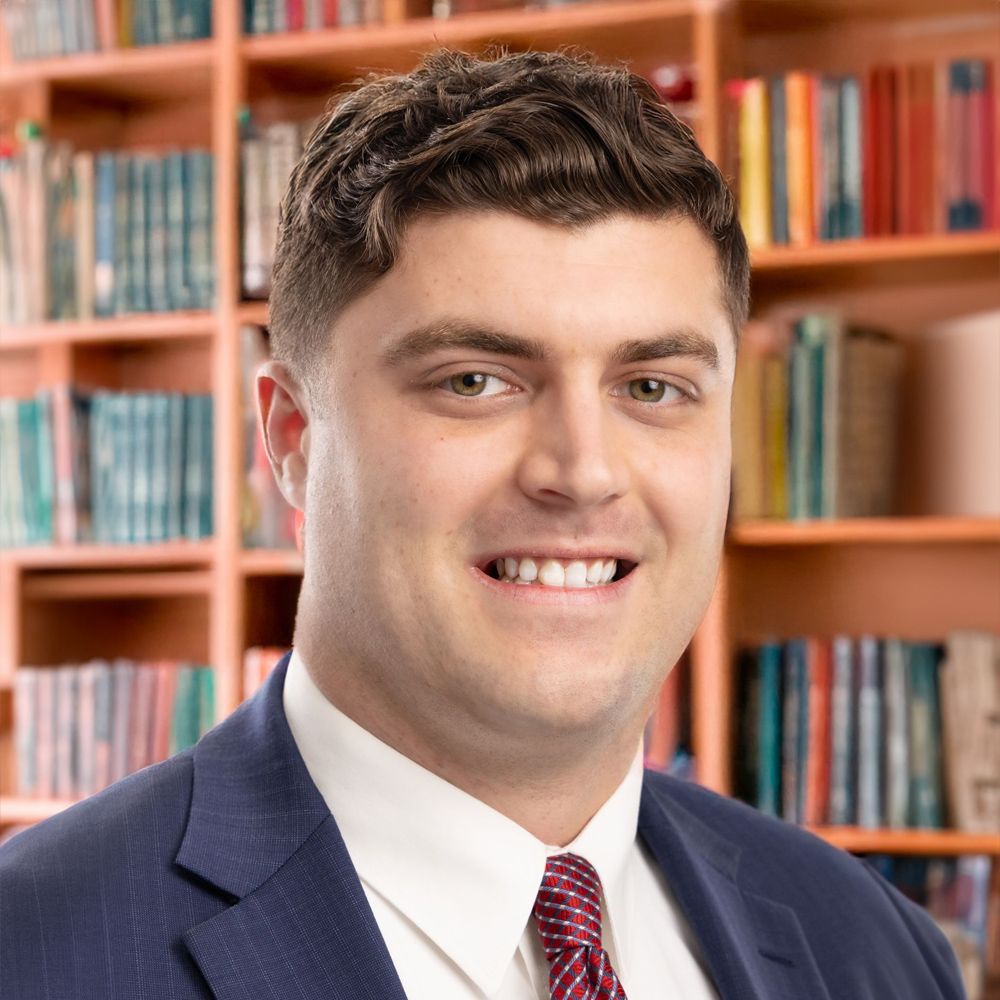 Smiling man in a suit with a book-filled library background.
