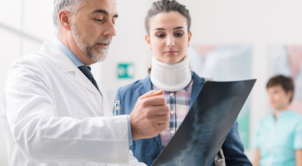 Doctor reviewing X-ray with patient wearing neck brace in hospital setting.