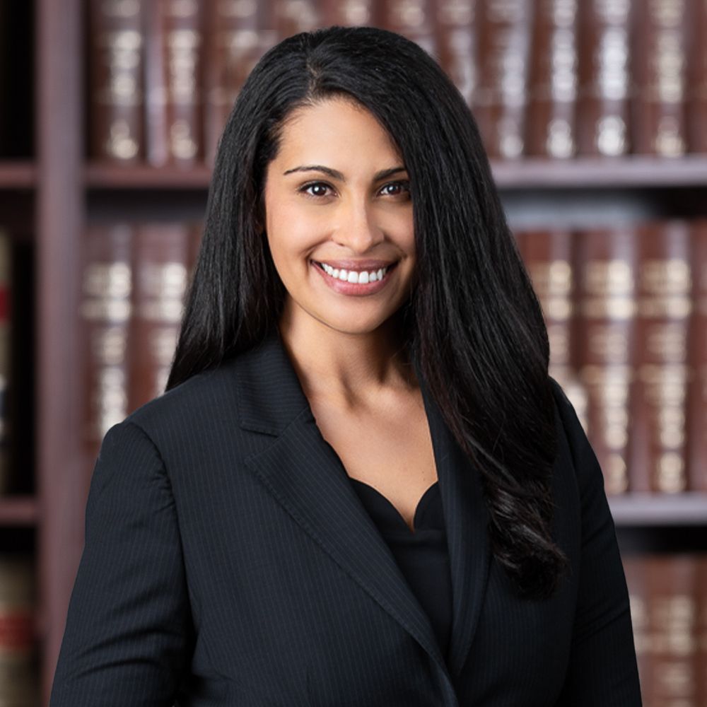 Smiling woman in a suit stands in front of bookshelf, conveying professionalism and confidence.