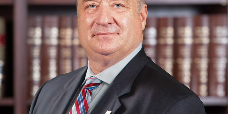 Professional man in a suit posing confidently in front of bookshelves in an office setting.