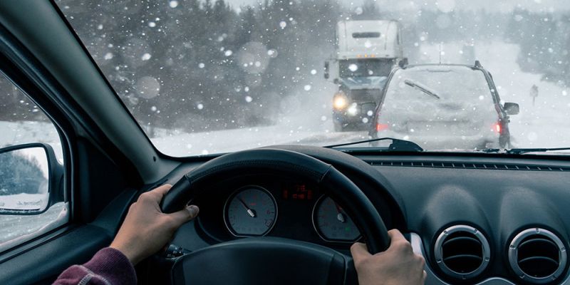 Driving in snowy weather, view from inside a car, surrounded by snow-covered vehicles and falling snowflakes.