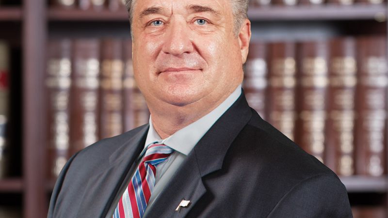 Professional man in a suit posing confidently in front of bookshelves in an office setting.