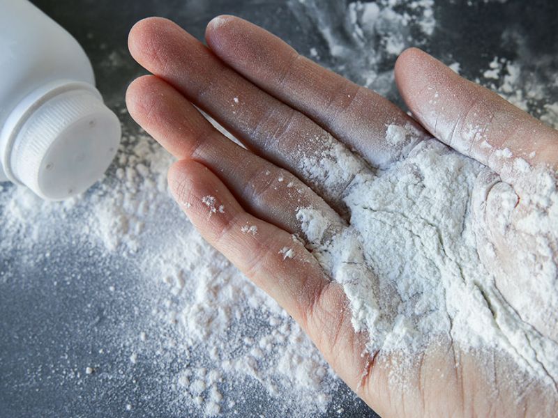 Hand holding talcum powder with bottle nearby on a dark surface.