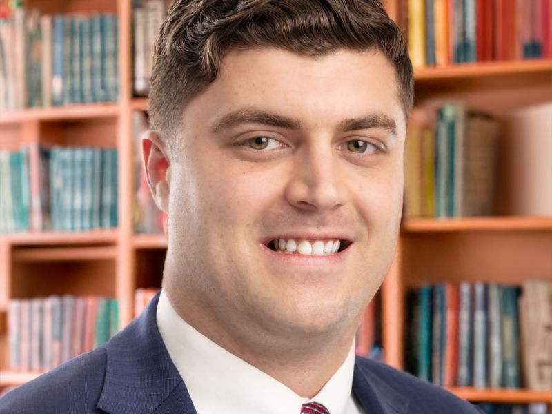 Smiling man in a suit with a book-filled library background.