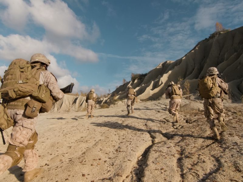 Soldiers in Iraq War advancing uphill under clear skies, showcasing military readiness and teamwork.