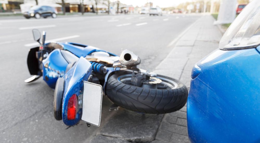 Blue motorcycle lying on the road after collision with blue car on city street.