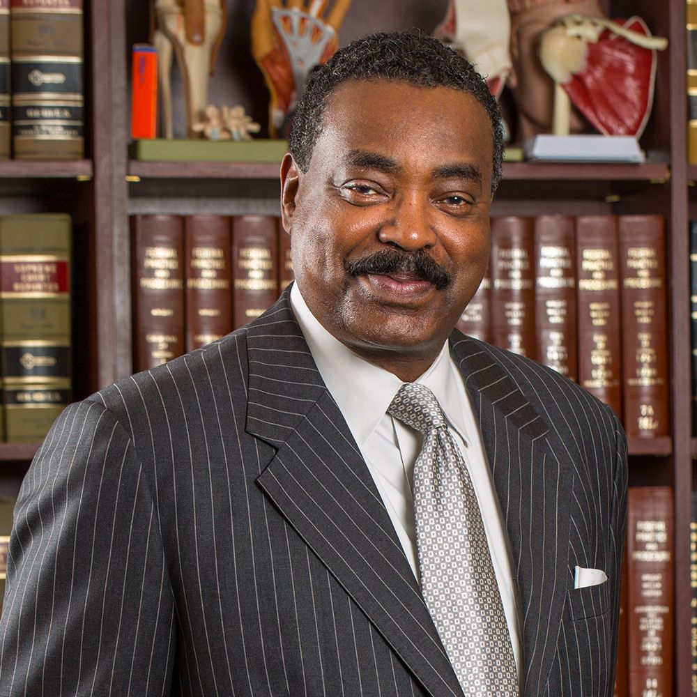 Professional man in a suit smiling in front of bookshelves with anatomical models, conveying expertise and knowledge.