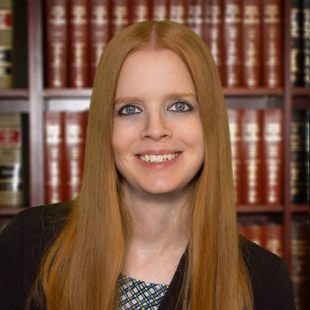 professional woman with long red hair smiling in front of bookshelves filled with legal volumes