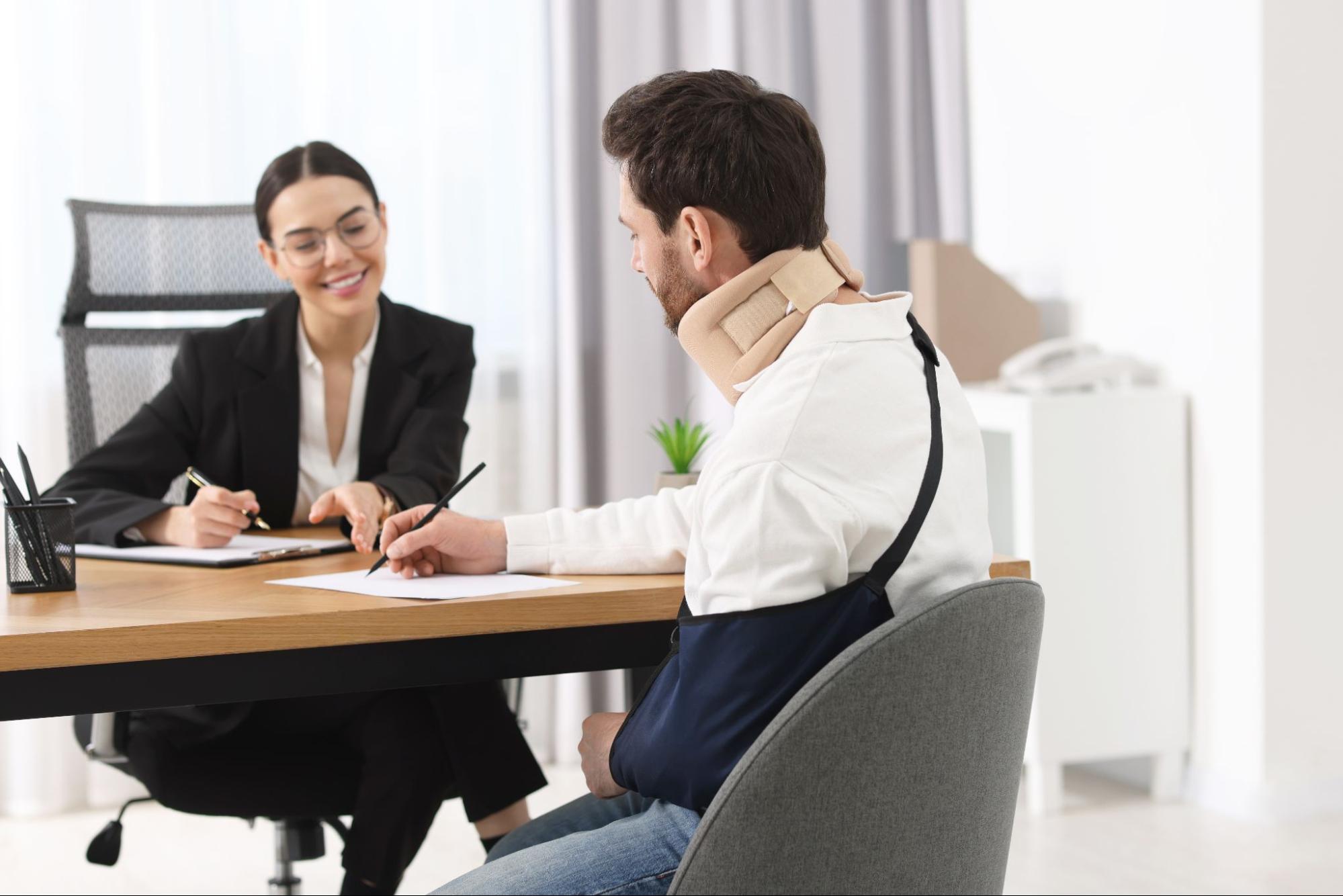 injured man consulting with lawyer in office about legal document wearing neck brace and arm sling