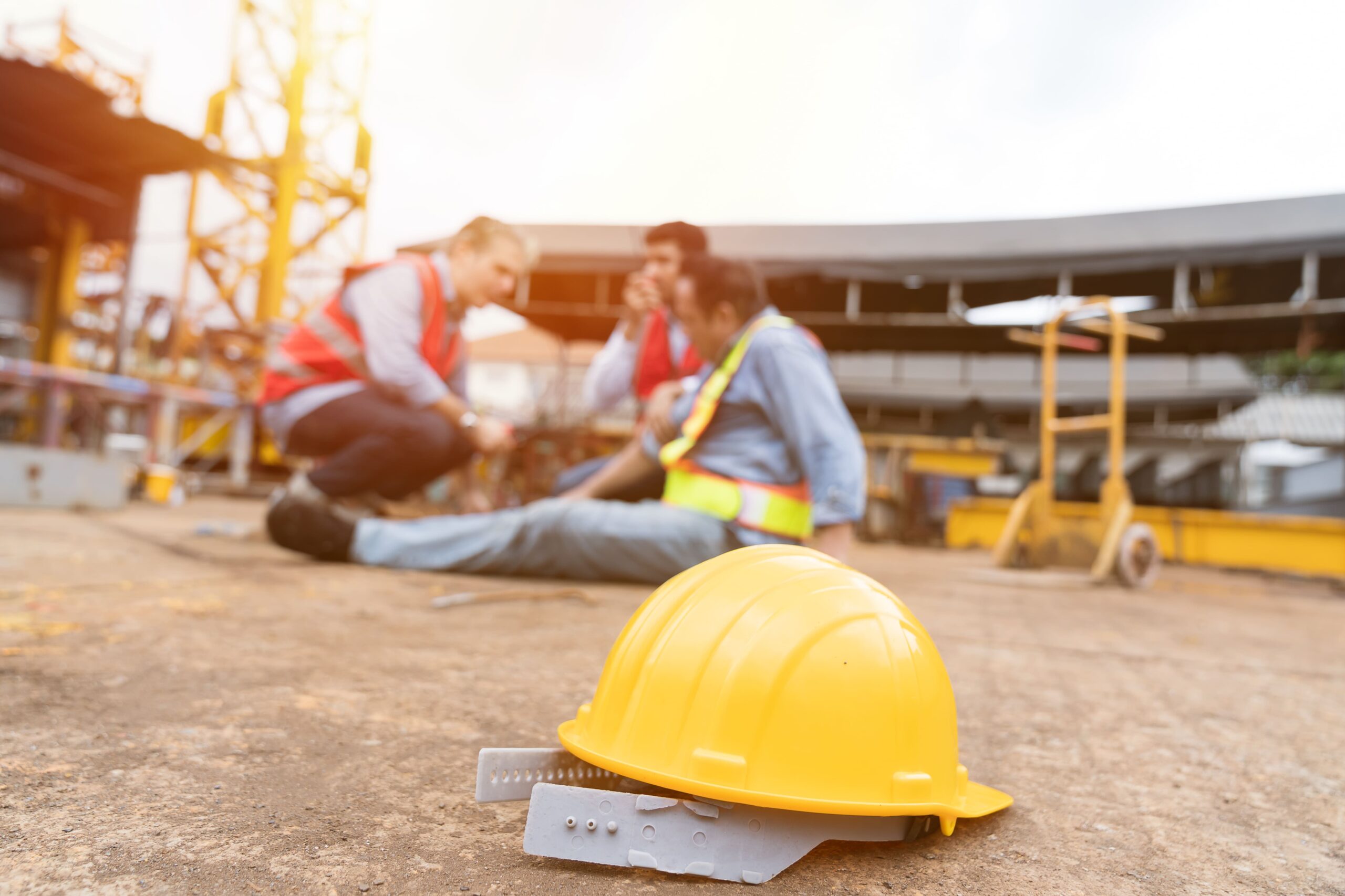 Yellow hard hat on the ground at a construction site with blurred workers in high-visibility vests in the background.